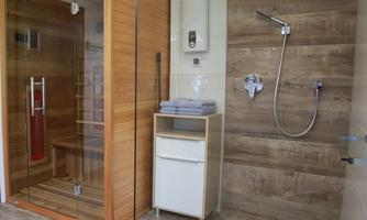 A modern shower with an open glass partition and a wooden sauna. The room is bright and elegantly designed with wooden and white elements.