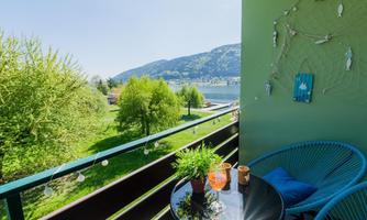 A cozy balcony with plants and a small table. In the background, a green landscape and a river can be seen.