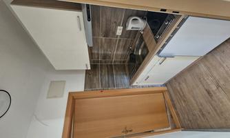 A small kitchen with modern white cabinets and wood laminate flooring. It features a sink, stove, and microwave.