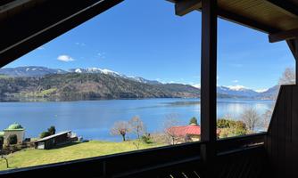 An impressive view of a tranquil lake, surrounded by mountains and trees. The clear sky and sunny landscape create a relaxed atmosphere.