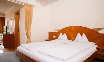 A simple room with two beds and wooden furniture. The room has orange curtains and a television.