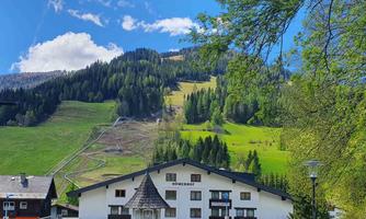 A picturesque village with a traditional building and a lovely surroundings. In the background, green mountains rise under a clear blue sky.