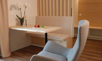 A modern room with a desk and a comfortable chair. The walls are light and there are plants as well as warm light.