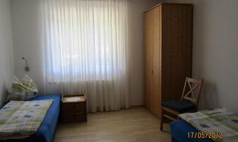 A simple room with two single beds and a wooden wardrobe. The light gently filters through the curtains.