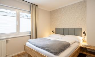 A cozy bedroom with a large bed and neutral colors. Large windows let in plenty of light and create an inviting atmosphere.