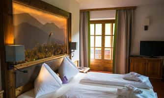 A cozy bedroom with two beds and a wooden landscape picture wall. Large windows let in a lot of light.