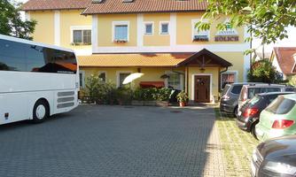 A guest house with a yellow facade and an entrance area. Several cars and a coach are parked in front of the house.