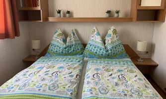 A cozy bedroom with two single beds and colorful bedspreads. On the wall, there are small plants and two bedside lamps.