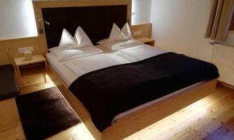 A modern bedroom with a large double bed and elegant wooden furnishings. Soft lighting creates a cozy atmosphere.