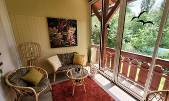 A cozy patio with rattan furniture and a small table. The large windows provide a view of the greenery.