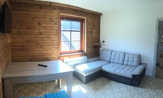 A cozy living room with wood paneling and a gray sofa. A table and a television complete the decor.