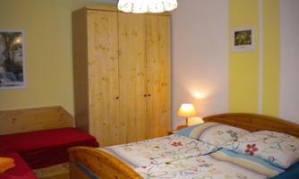 A cozy bedroom with a large double bed and a single bed. The room has pleasant lighting and bright walls.