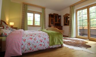 A cozy bedroom with floral decor on the bed. Large windows let in plenty of daylight and provide access to a balcony.