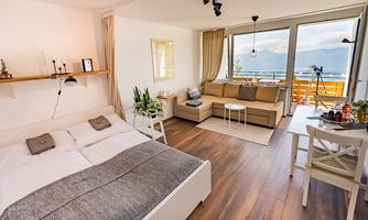 A modern living room with a comfortable bed and a cozy seating area. Large windows provide a beautiful view of the surroundings.
