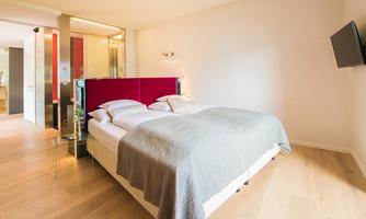 A modern bedroom with a large double bed and elegant walls. The floor is wooden, and there is a television on the wall.