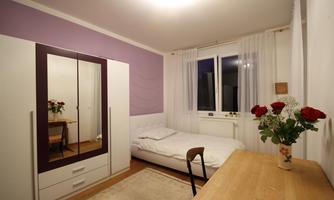 A cozy bedroom with a white bed and a large wardrobe. Fresh flowers are on the table and there is a view from the window.