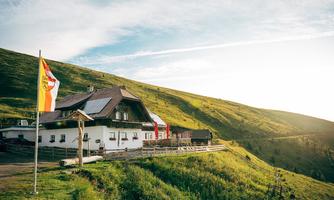 A beautiful alpine house on a green meadow, surrounded by gentle hills. The sun is shining and there is a light breeze in the flags.
