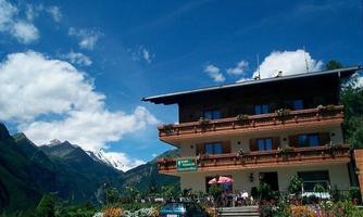 A picturesque mountain hotel with blooming flowers and a clear blue sky. Majestic mountains can be seen in the background.