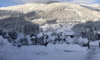 A winter landscape with snow-covered mountains and trees. The sky is partly cloudy, and the scene is calm and peaceful.