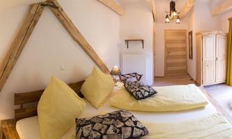 A cozy bedroom with two beds, yellow pillows, and wooden details. Large windows provide plenty of light and coziness.
