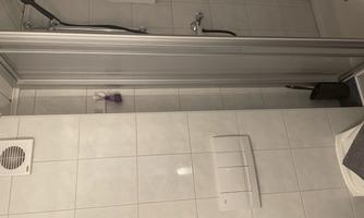 A small bathroom with a shower and white tiles. There is a towel rack and a shower head.