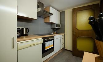 A modern kitchen with white cabinets and wooden shelves. Kitchen appliances and a window to the door are visible on the countertop.