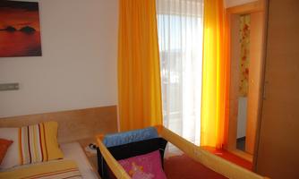 A bright room with a bed and colorful curtains. In the corner there is a children's bed.