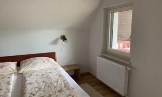 A cozy bedroom with a large bed and floral bedding. Next to the bed is a window that lets in daylight.