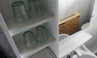 A bathroom shelf with three glass cups and a towel. In the background, white tiles and a radiator are visible.