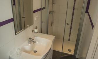 A modern bathroom with a shower and a sink. The walls are brightly tiled, and there is a large mirror.