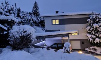 A snow-covered house in a quiet winter landscape. The garden is covered with snow and it is dusk.