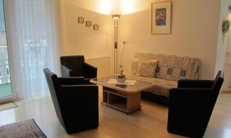 A cozy living room setup with two black armchairs and a corner sofa. A table with a plant stands in the center of the room.