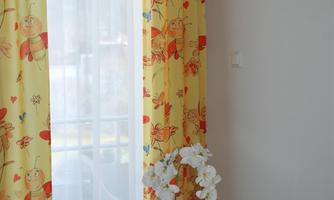A bright room with colorful yellow curtains and a small table. On the table, there is a flower in a pot and a yellow leaf.