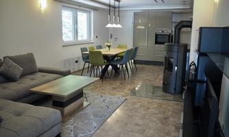 A modern living room with a gray sofa and a wooden table. In the background, there is a dining area with a large table and chairs.