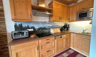 A modern kitchen with wooden cabinets and a refrigerator. In the background, there is a landscape painting depicting a mountainous scenery.