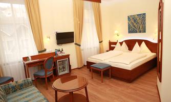 A cozy hotel room with a double bed, a desk, and a comfortable armchair.  
Large windows provide plenty of daylight and a bright atmosphere.