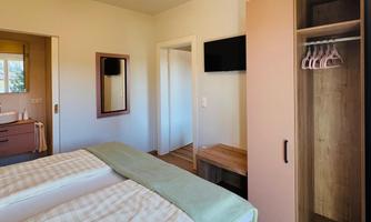 A cozy bedroom with a double bed and soft colors. The room has a television, a wardrobe, and pleasant lighting.
