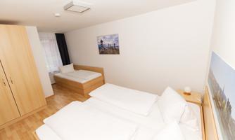A bright room with two beds and a single bed. The walls are simply painted, and there are wooden wardrobes as well as decorations on the walls.