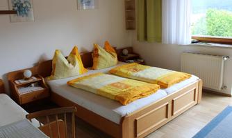 A cozy bedroom with a double bed and colorful pillows. The room is bright and offers a view outside.