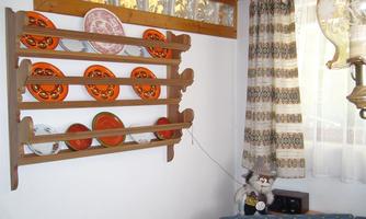 A cozy room with a shelf displaying colorful plates. Next to the shelf stands a chair with a decorative pillow.