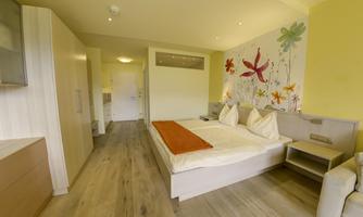 A modern bedroom with a double bed and a colorful wall design. The decor is bright and inviting, featuring wooden flooring and a small seating area.