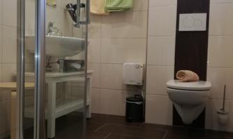 A modern bathroom with a shower, sink, and toilet. The walls are brightly tiled and there are green towels.