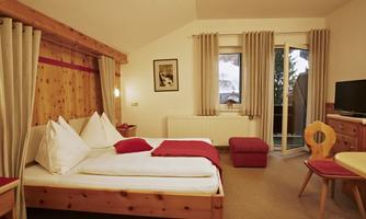 A cozy room with wooden details, two beds, and a TV. The room has large windows with access to a balcony.
