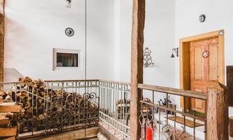 A cozy interior with wooden beams and an open staircase area. The room has white walls and a warm, inviting atmosphere.