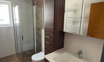 A modern bathroom with a shower, a sink, and wooden cabinets. The walls are brightly tiled and the floor has a wood look.