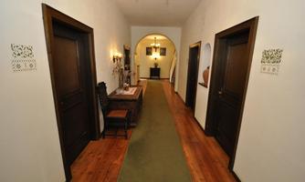 A flat hallway with wooden doors and a green carpet. At the end of the hallway is an arch and subtle lighting.