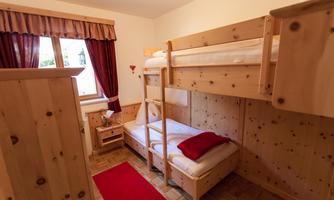 A cozy room with wooden furniture and a bunk bed. The room is bright and friendly, with a red carpet and curtains.