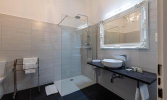 A modern bathroom with a glass shower and elegant tiles. The sink is placed on a simple table, accompanied by a large mirror.