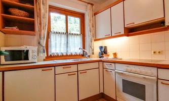A bright kitchen with wooden cabinets and a window that lets in plenty of daylight. On the countertop, a microwave and a stove are visible.