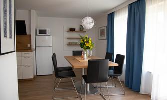 A modern dining room with a wooden farmhouse table and black chairs. A bouquet of flowers and large windows create a bright, inviting atmosphere.